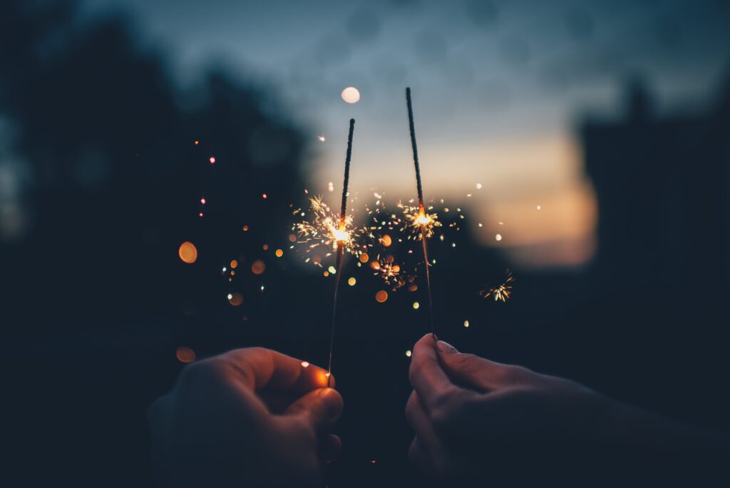 Two hands with lit sparklers in front of a sunset.