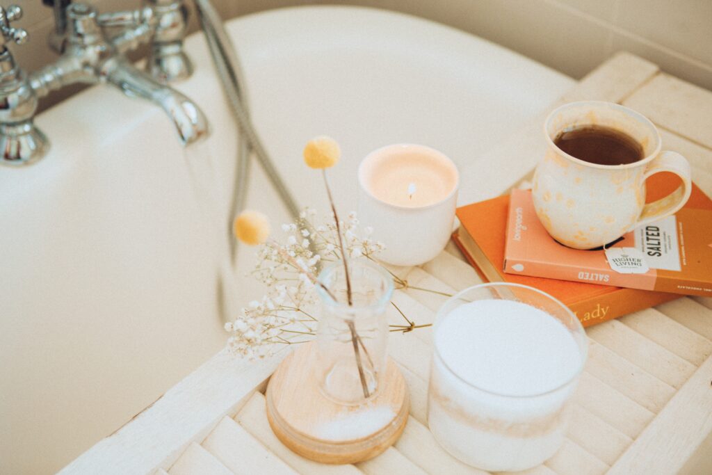 A white bathtub with a small vase of flowers, a cup of tea and a white candle.
