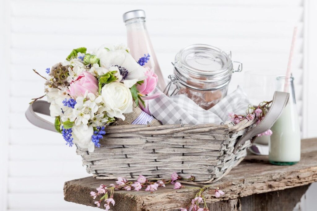 Woven basket with a bottle and a jar visible with a bouquet of light colored flowers.